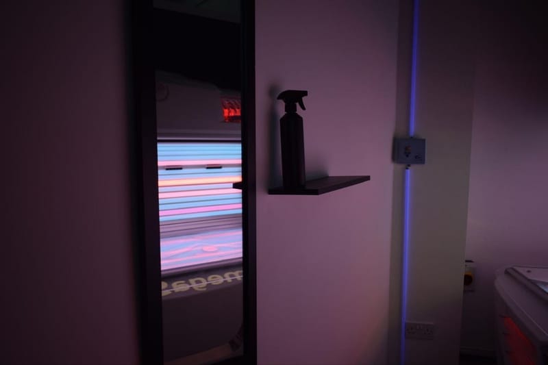 Dim treatment room with a sunbed glowing pink and blue behind a black spray bottle